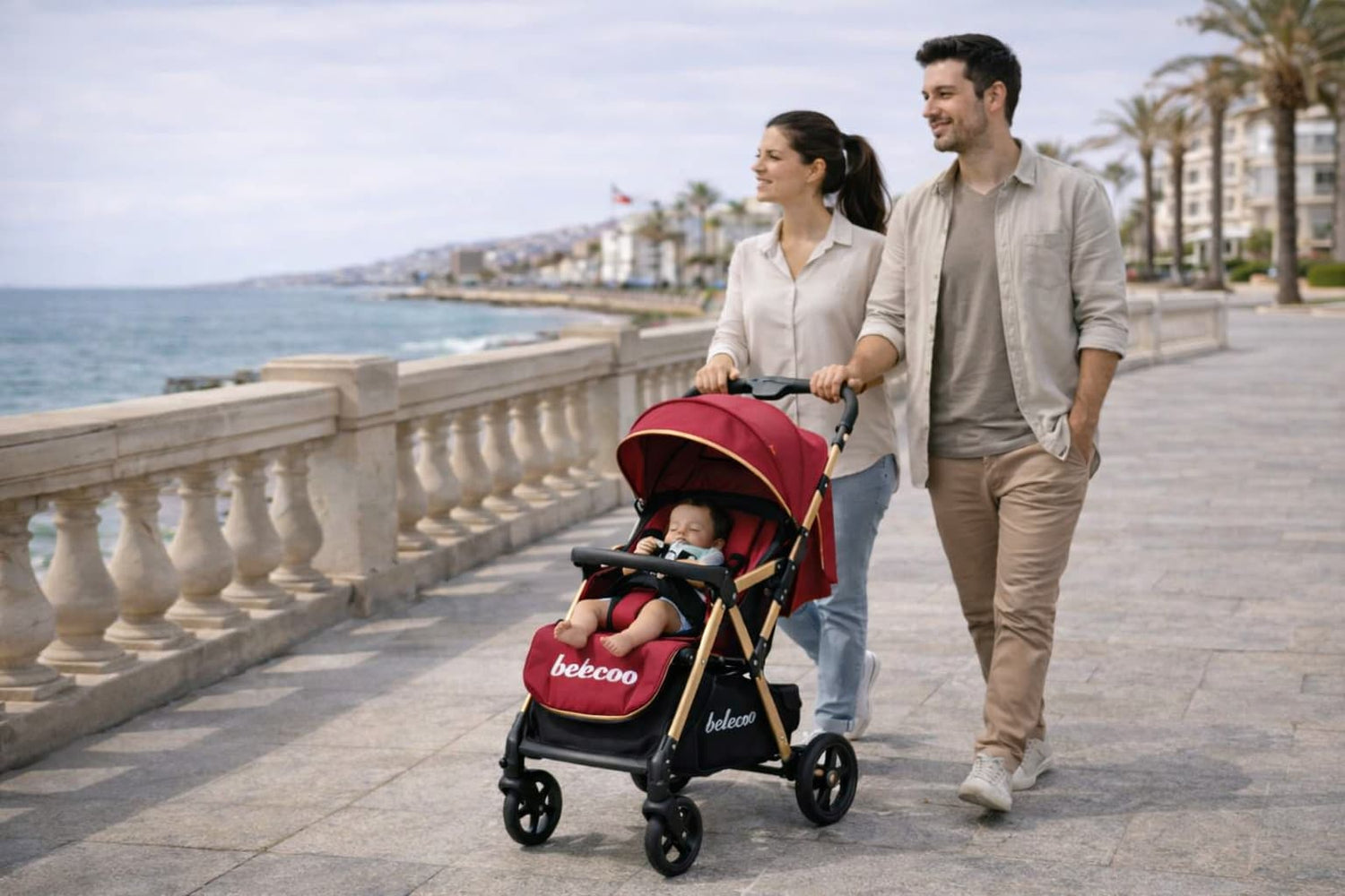 Parents promenant leur bébé dans une poussette rouge en bord de mer